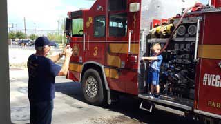 Young boy standing on fire truck getting his picture taken