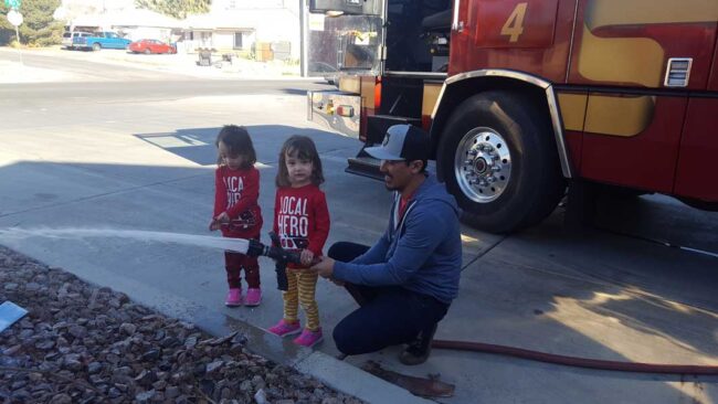 Fireman showing toddler twins the fire hose