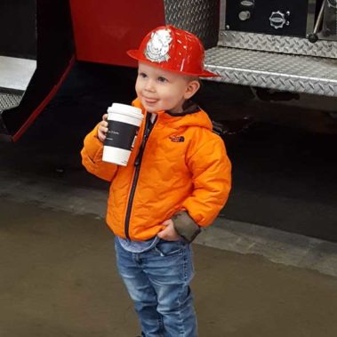 Young boy happy holding a drink in front of the fire truck