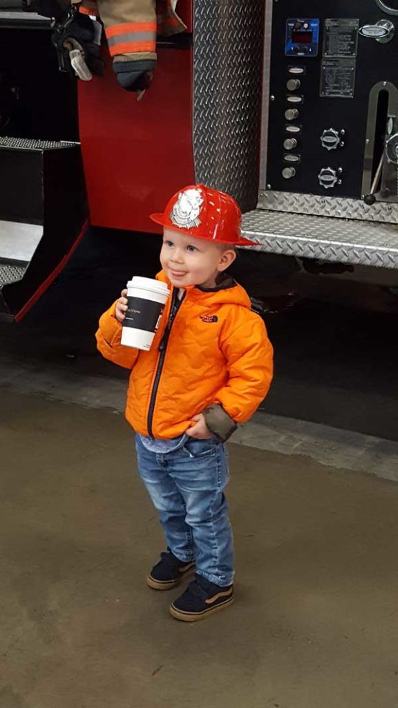 Young boy happy holding a drink in front of the fire truck