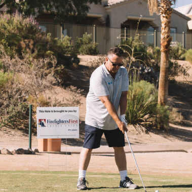 A guy getting ready to swing with Firefighters First Credit Union Sponsored Hole sign